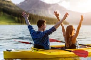 Confident young caucasian couple kayaking on river together with sunset in the backgrounds. Having fun in leisure activity. Romantic and happy woman and man on the kayak boat. Sport, relations concept