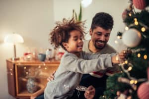 Cute african american girl decorating Christmas tree with dad.